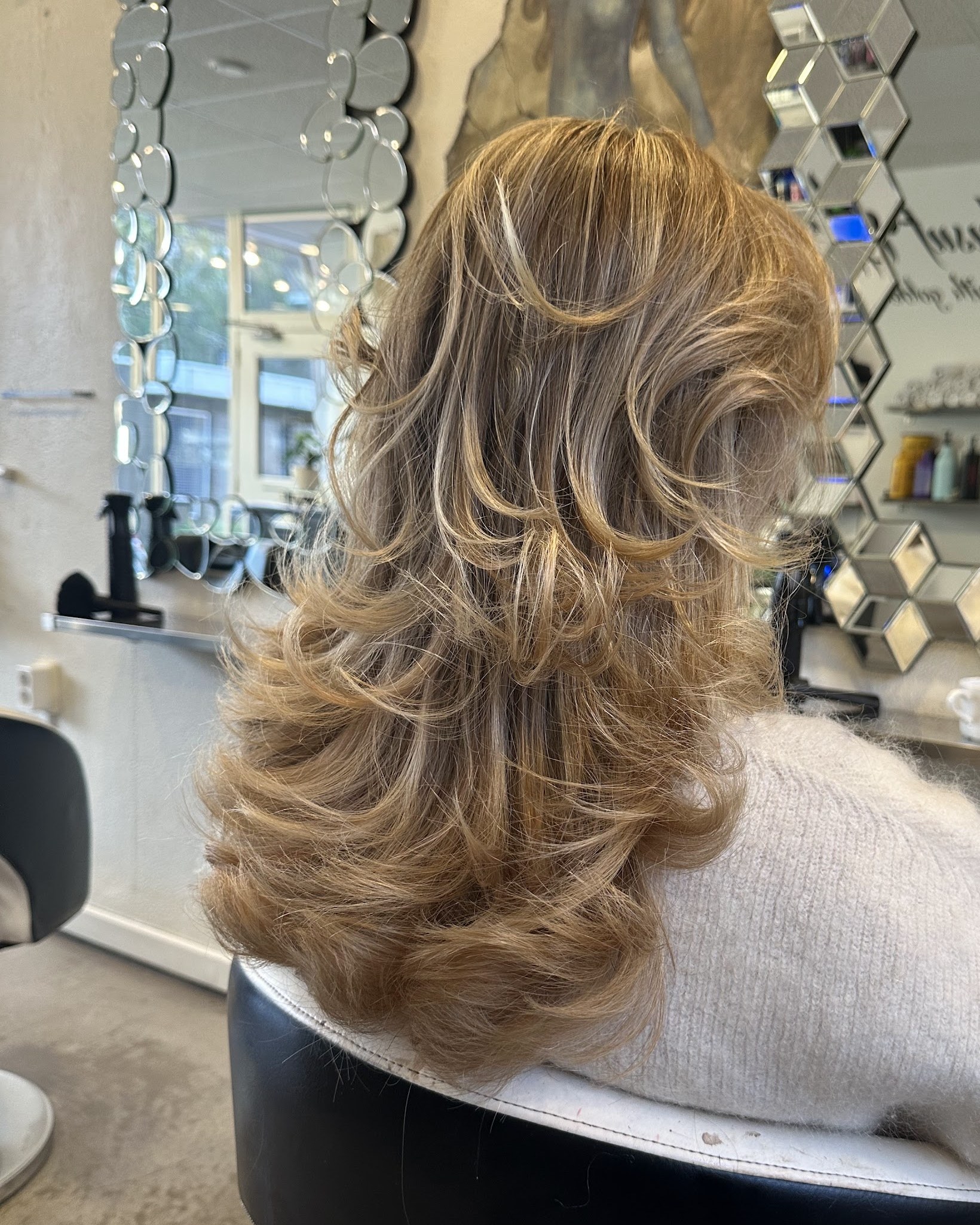 Lang blond haar in laagjes, geföhnd, van achteren gezien in de salon met de spiegelwand